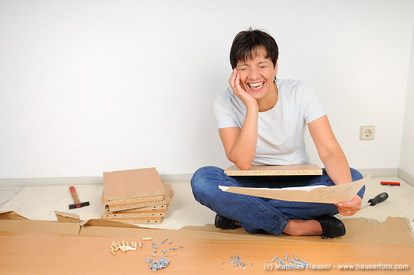 Lachende Frau beim Möbel zusammenbauen, Lesen der Anleitung - Laughing woman assembling furniture, reading the instructions
