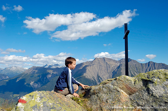 Junge schaut auf ein Kreuz in den Bergen, Riederhorn, Wallis, Schweiz, Europa - Boy is looking at a cross, Riederhorn, Valais, Switzerland, Europe