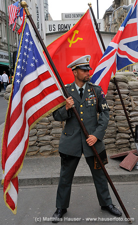 A man in uniform poses for tourists at Checkpoint Charlie, the former border crossing in Berlin, Germany. There are flags of the USA, the former Soviet Union and the United Kingdom which represents th