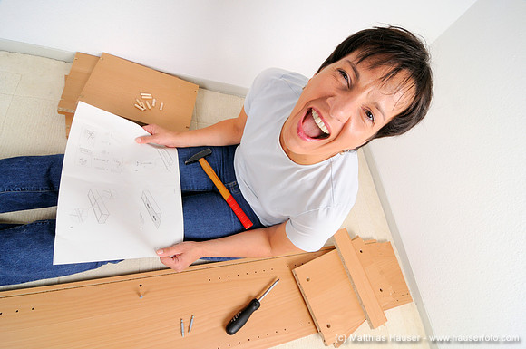Schreiende frustrierte Frau beim Möbel zusammenbauen, Lesen der Anleitung - Frustrated woman assembling furniture and screaming, reading the instructions